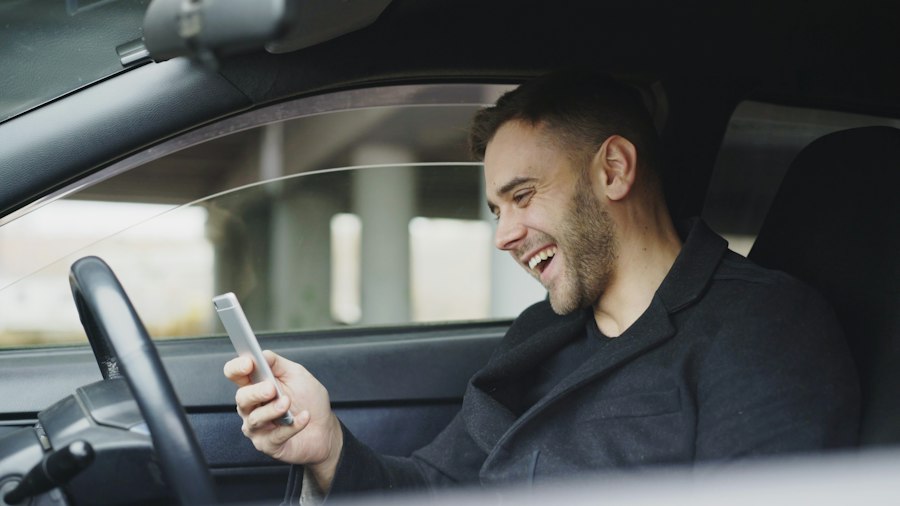 Zufriedener Außendienstler schaut im Auto lächelnd aufs Handy
